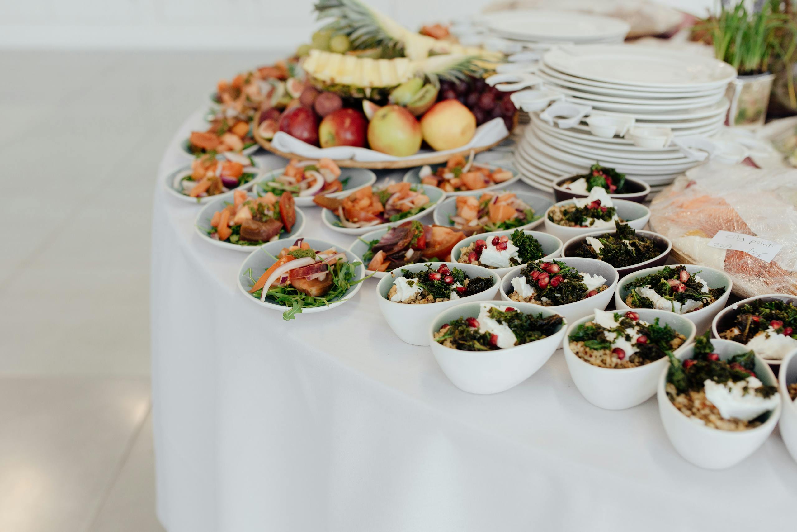 Bowls with bulgur and salads with fish served on white table with dishware and various ripe fruits during festive event